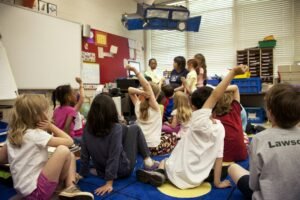kids sitting in a classroom, some raising their hands