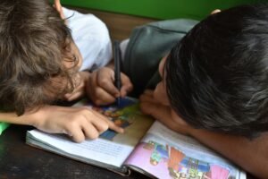 two kids reading and drawing in a book with their heads down