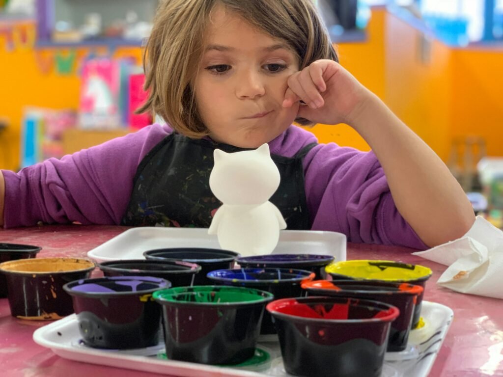 kid looking at small cups of paint to pick a color to paint her toy