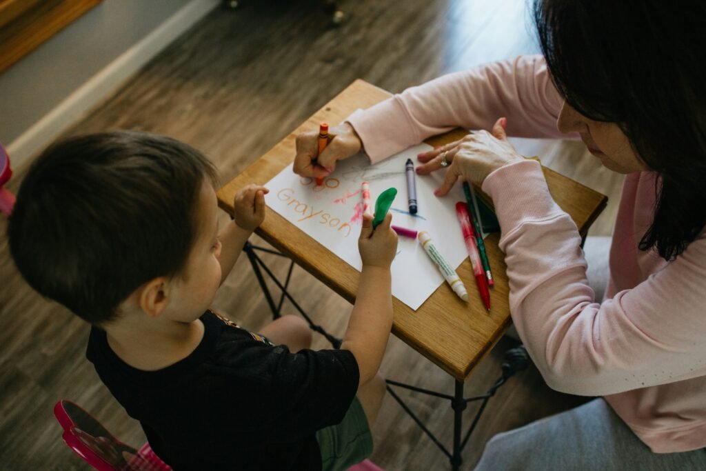 toddler drawing on a paper and an adult helping him