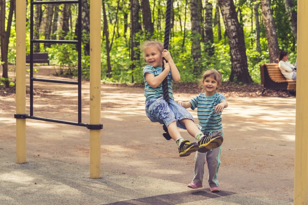 two little girls playing in a playground on a rope swing